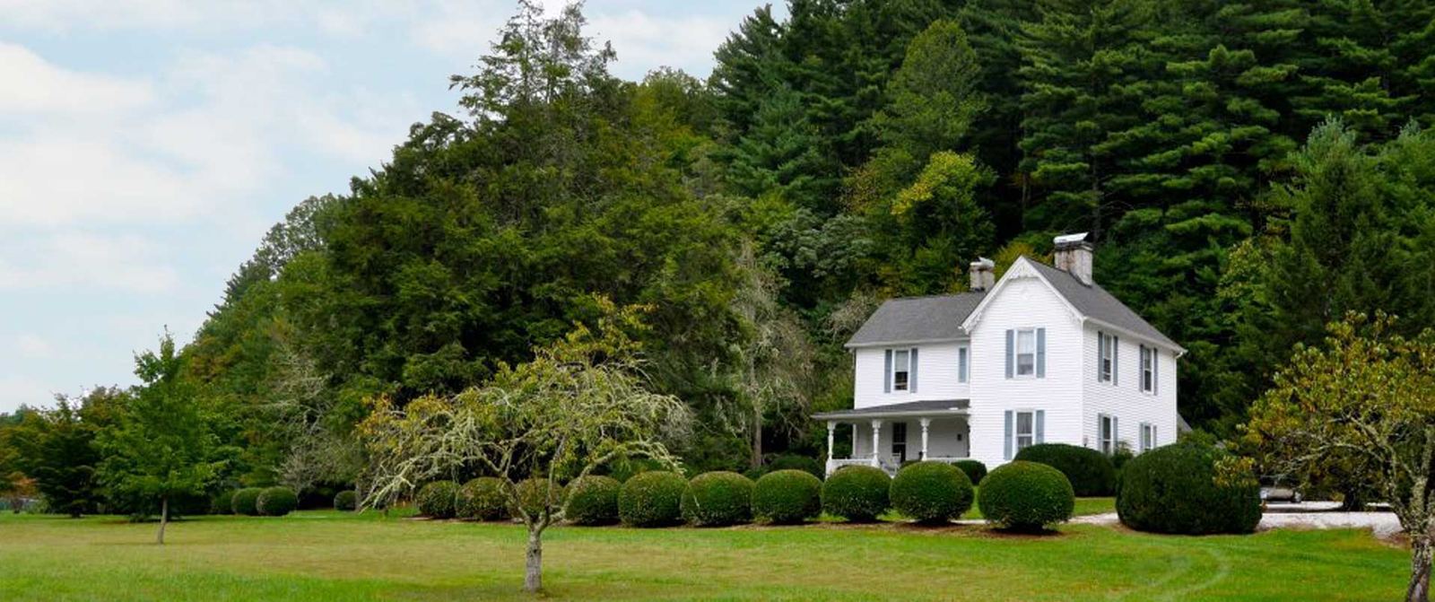 Key Falls Inn, a white Victorian house on a green lawn below the forested ridge